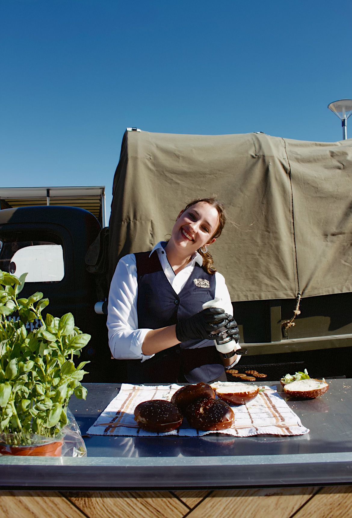 Lachende vrouw bereidt hamburgers bij een vintage groene vrachtwagen.