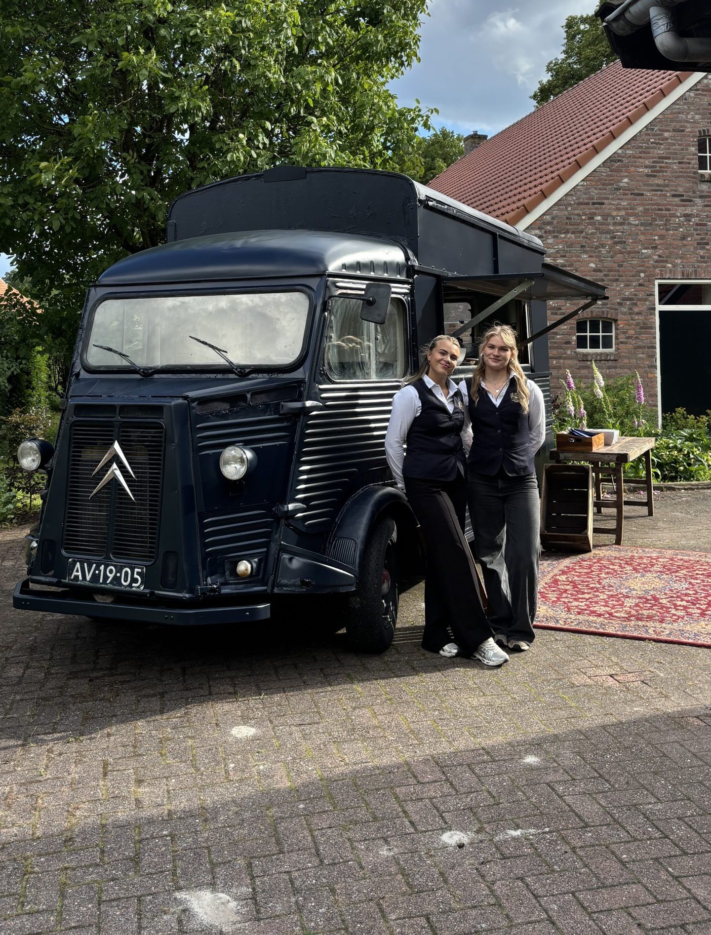 Twee vrouwen glimlachen voor een donkerblauwe vintage Citroën foodtruck.