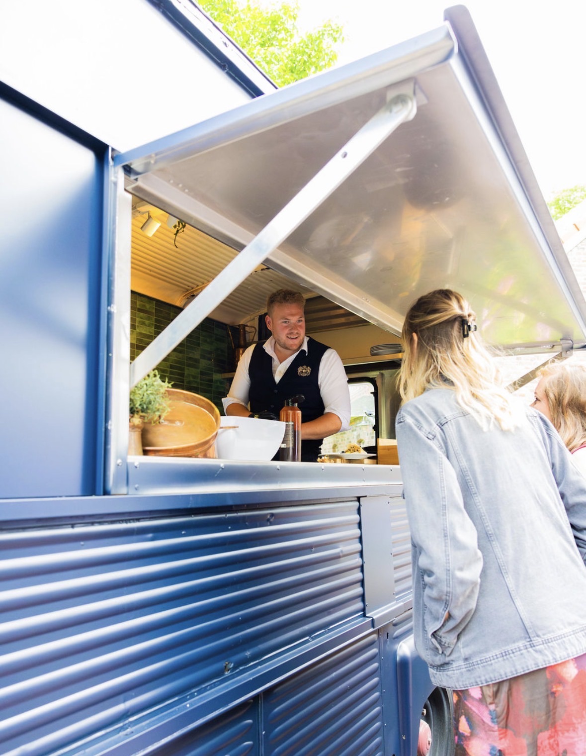 Een glimlachende kok in een blauwe vintage Citroen foodtruck.
