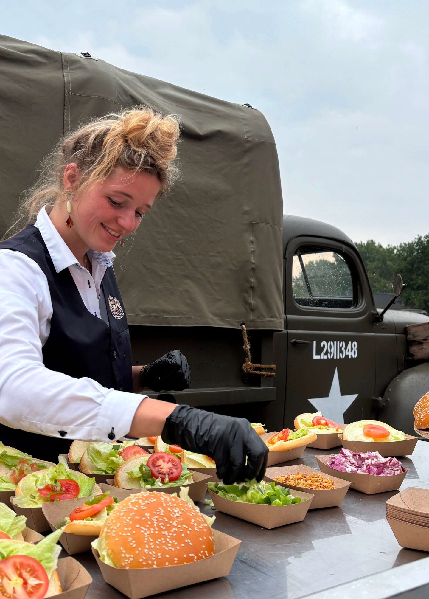 Vrouw bereidt hamburgers voor een vintage legerfoodtruck.