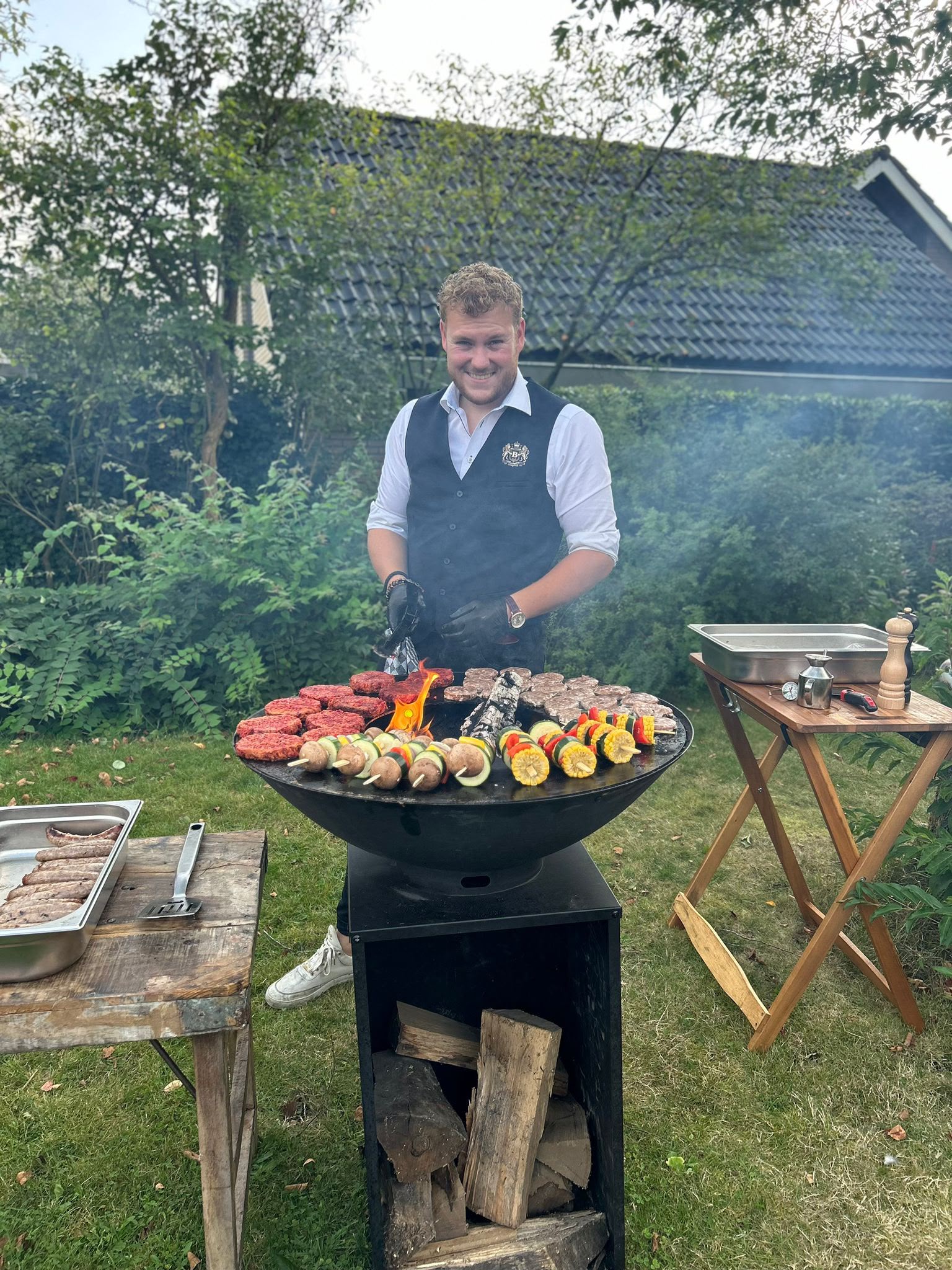 Man grilt hamburgers en groentespiesjes in tuin