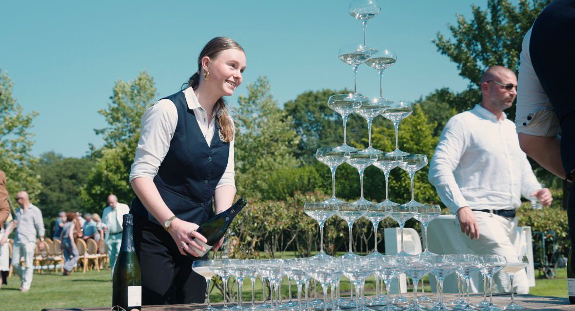 Serveerster vult champagnepiramide op tuinfeest
