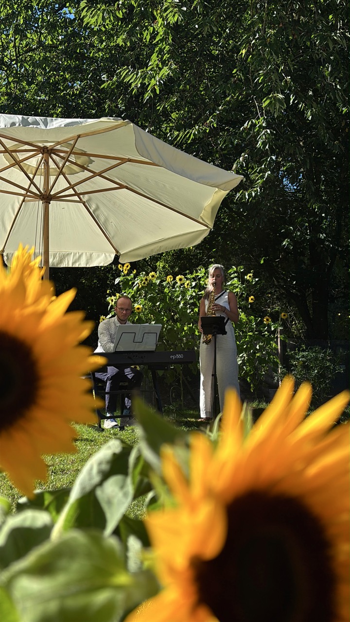 Saxofoniste en pianist spelen buiten tussen zonnebloemen