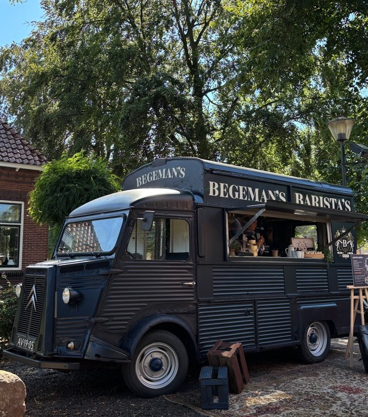 Donkerblauwe mobiele koffiebar onder groene bomen