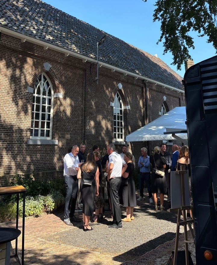 Mensen verzamelen bij een bakstenen kerk onder bomen